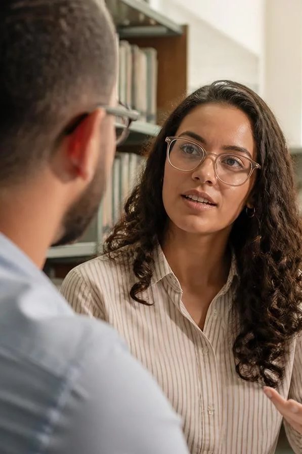 Duas participantes de pé conversando no corredor entre prateleiras de livros